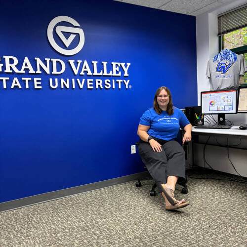 Sam Purifoy sitting at a desk with a blue wall behind her